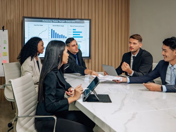 Five professionals engaged in a sales strategy meeting with charts and sticky notes.