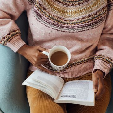 Person reading a book with coffee in hand.