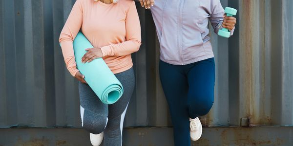 Two women in workout clothes smiling and holding fitness gear.