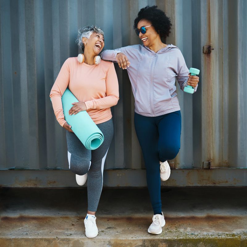 Senior women, exercise and laughing, cool and urban with workout equipment, friends and fun training together. Active female people, fitness fashion and yoga mat with dumbbell, sportswear and comedy