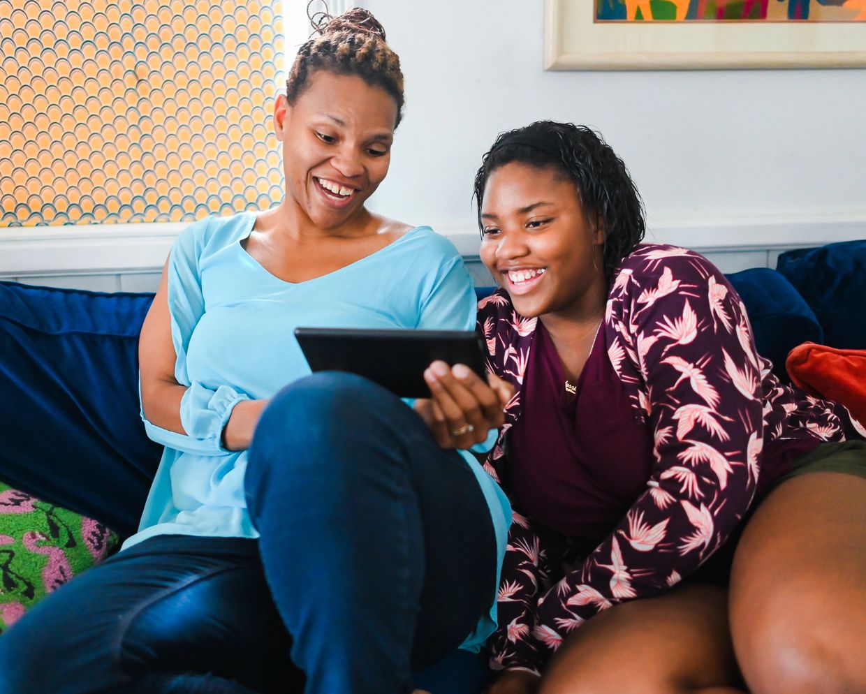 Two women happily looking at a tablet together on a couch.