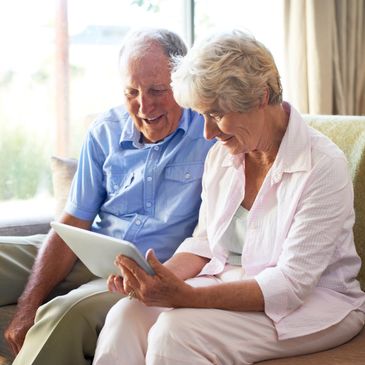 Elderly couple enjoying a tablet together on a sofa.