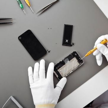Technician repairing smartphone with precision tools wearing white gloves.