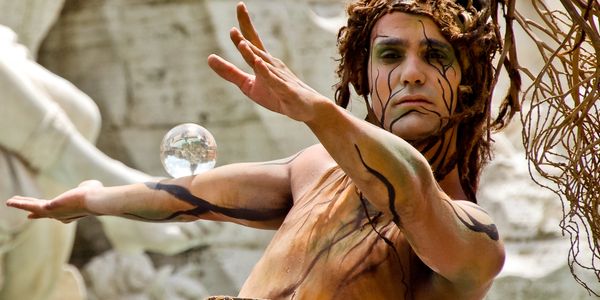 Artista performático com maquiagem teatral e bola de cristal.