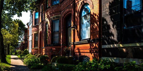 Sunlit brick townhouses along a tree-lined sidewalk.