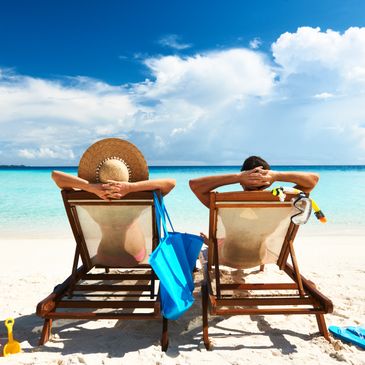 Couple relaxing on beach chairs facing the turquoise ocean under a bright sky.