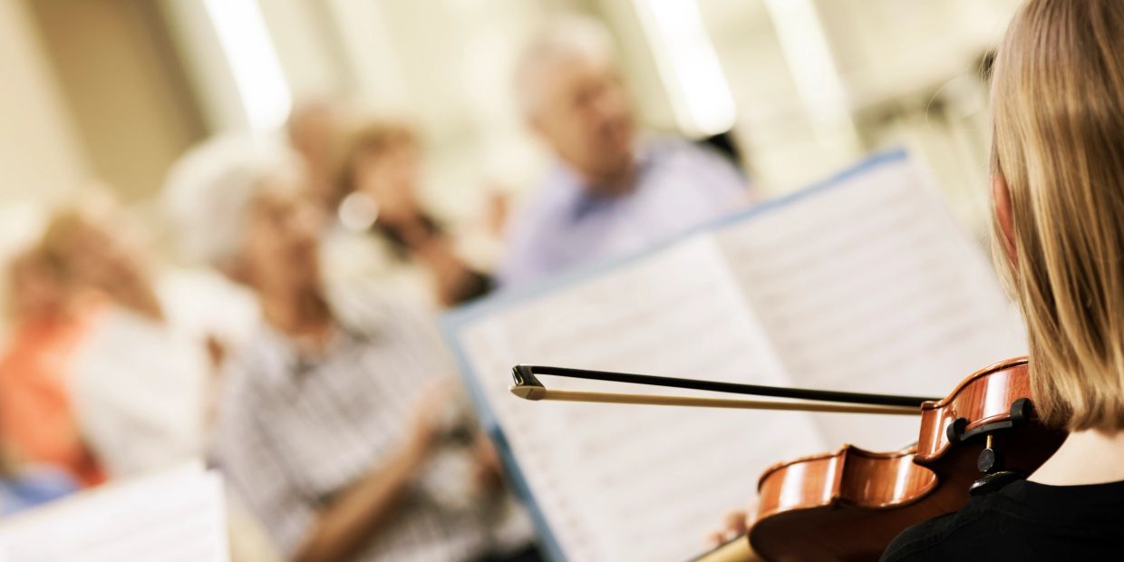 Violinist playing for an attentive elderly audience in a cozy setting.