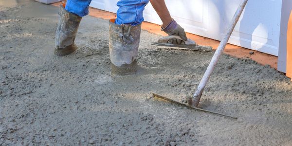 Worker smoothing wet concrete on the ground.