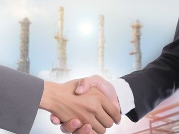 Two people shaking hands with an industrial plant in the background.