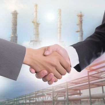 Two businesspeople shaking hands in front of an industrial plant.