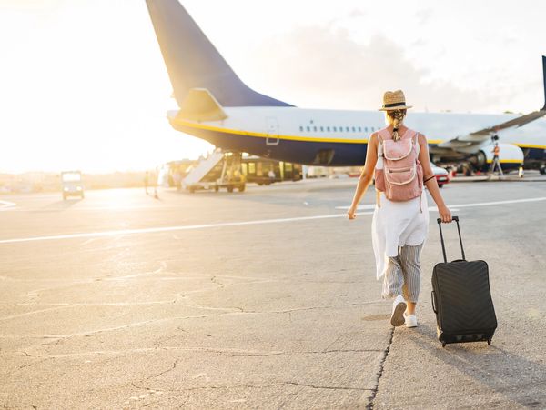 Traveler walking toward airplane with luggage at sunset.