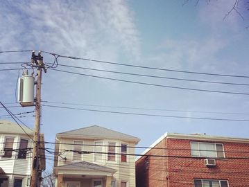 Residential buildings under a partly cloudy sky with power lines overhead.