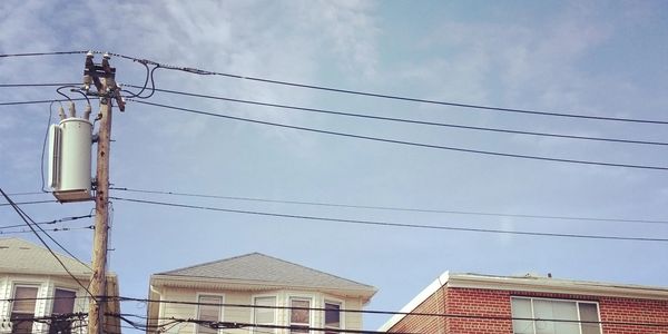 Power lines and utility pole above residential buildings under a clear sky.