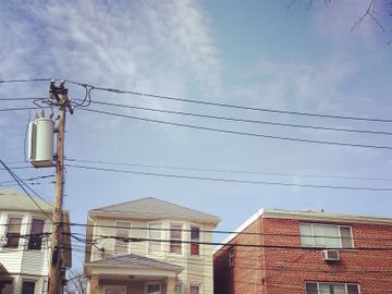 Residential buildings under a partly cloudy sky with power lines overhead.