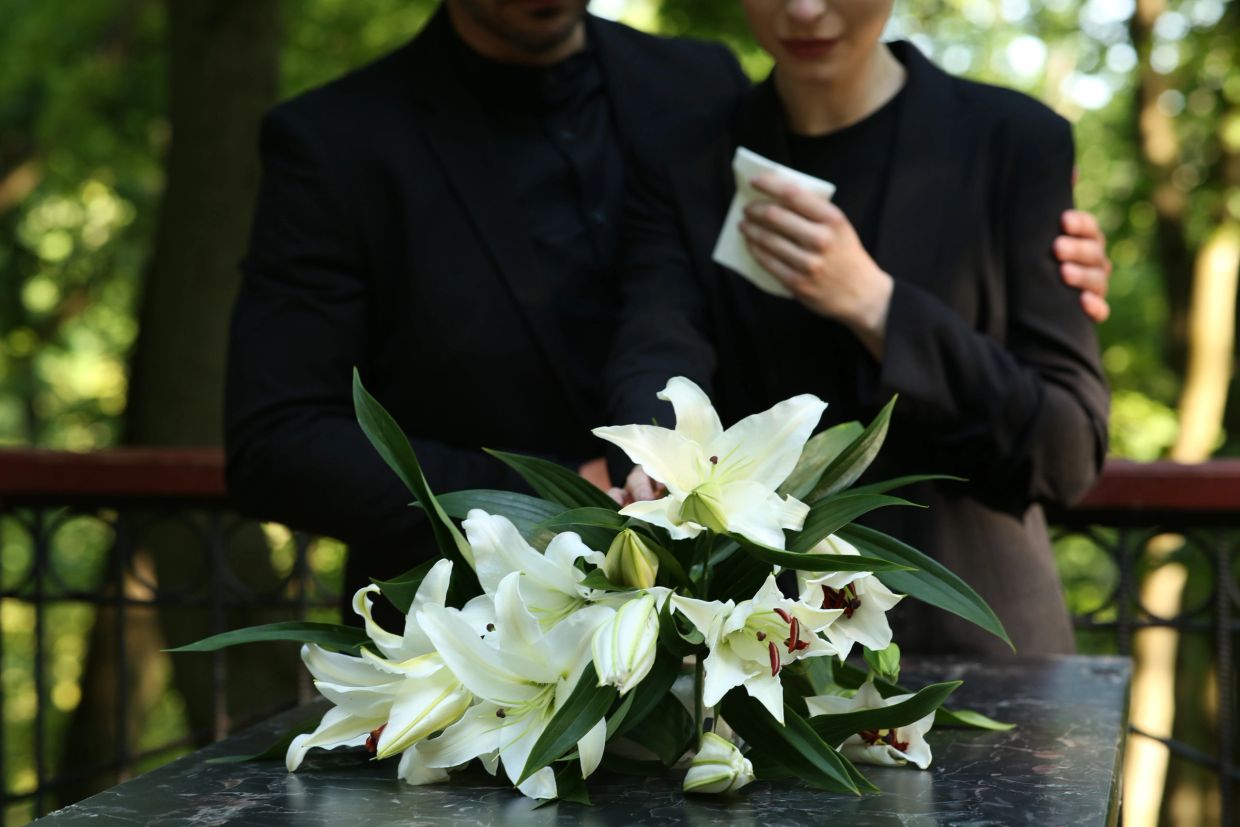 Couple mourning with white lilies at funeral.