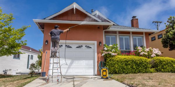 Man power washing house exterior from ladder.