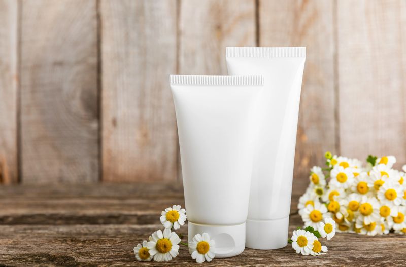 Open jar of moisturizing cream for face, body and hands with a chamomile flower on a light background. Herbal dermatological cosmetic hygiene cream. Natural cosmetic product. Beauty concept. MOCKUP
