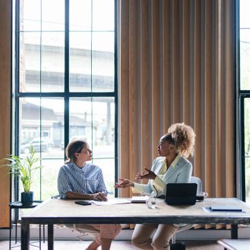 Two women engaged in a discussion at an office table.