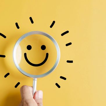 Magnifying glass highlighting a smiling sun drawing on yellow background.