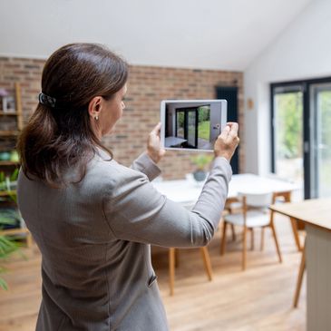 Woman photographing a modern dining area with a tablet indoors.