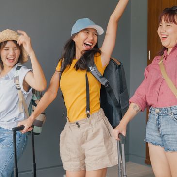 Three cheerful women with backpacks and suitcases celebrating travel plans.