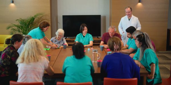 Healthcare workers and elderly people gathered around a table in a care facility.