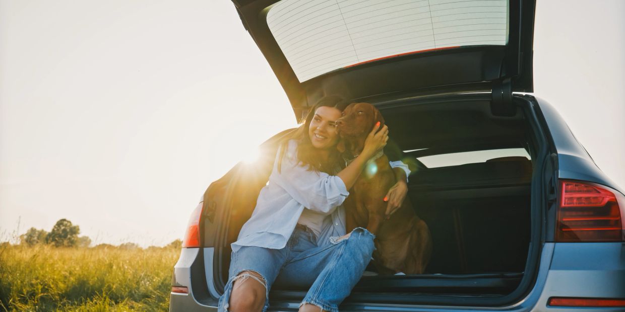 Woman hugs dog in car trunk during sunset.