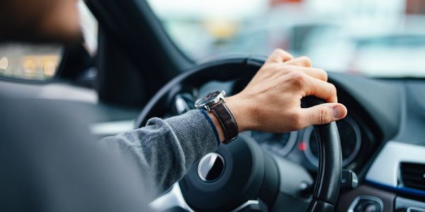 A person wearing a watch driving a car, holding the steering wheel.