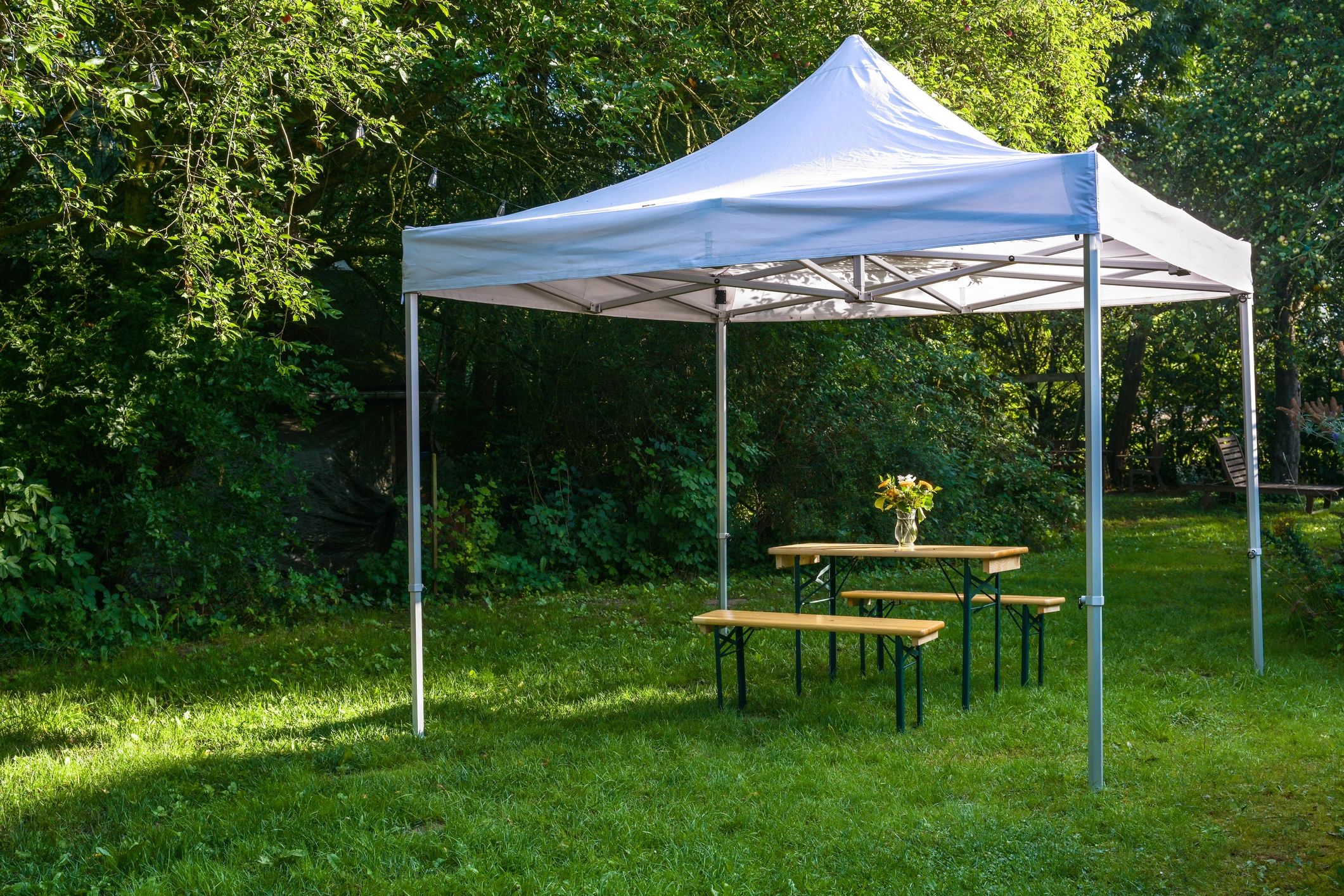 White canopy tent with picnic table and flower vase in a garden.