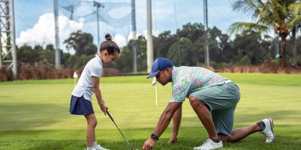 Man teaching young girl to play golf on a sunny day.