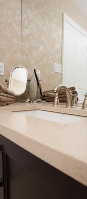 Elegant bathroom counter with beige floral wallpaper and silver fixtures.