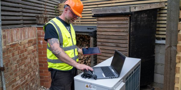 Worker in safety gear checks equipment using a laptop and phone.