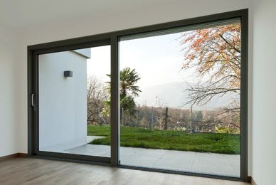 Empty room with wooden floor and large glass sliding door overlooking greenery.