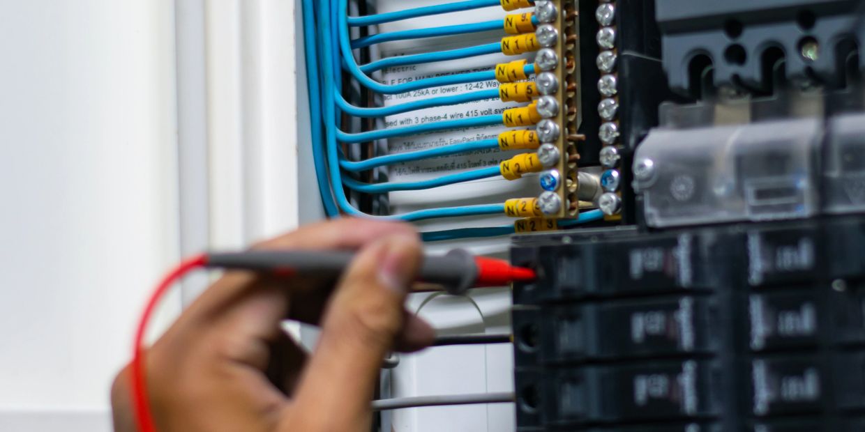 Hand using a tester on an electrical panel with organized blue wires.