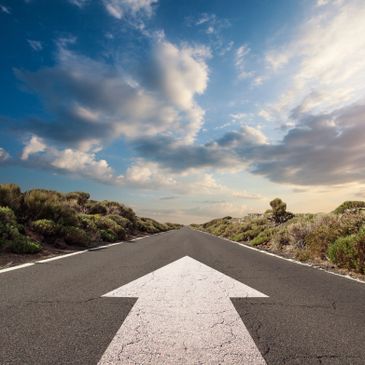 Straight road with a large white arrow pointing forward under a partly cloudy sky.