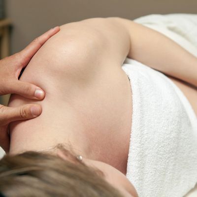 A person receiving a shoulder massage while lying down wrapped in a white towel.