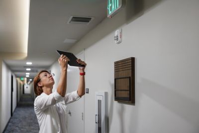 Woman inspecting a ceiling device with a tablet.