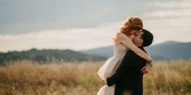Bride and groom lovingly embracing outdoors with mountains in the background.