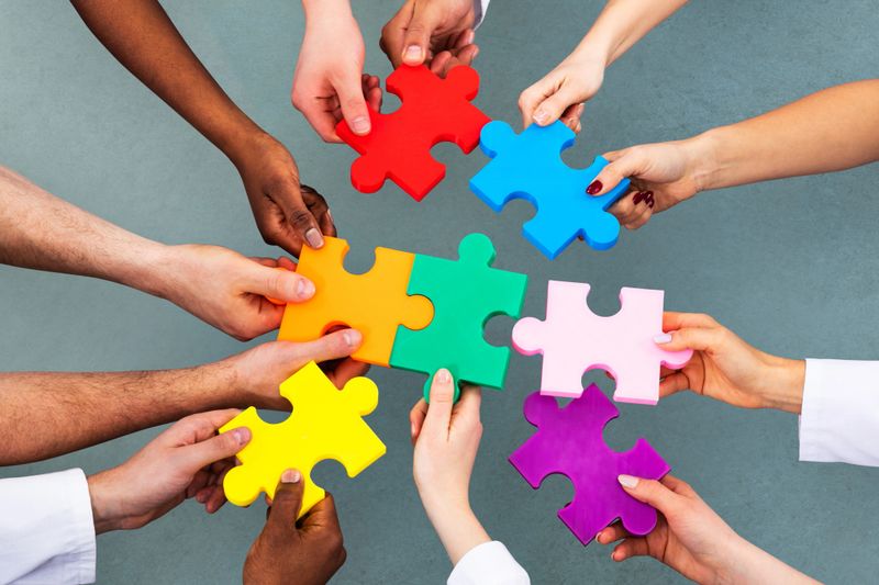 High Angle View Of Medical Team Solving Colorful Jigsaw Puzzle Against Grey Background
