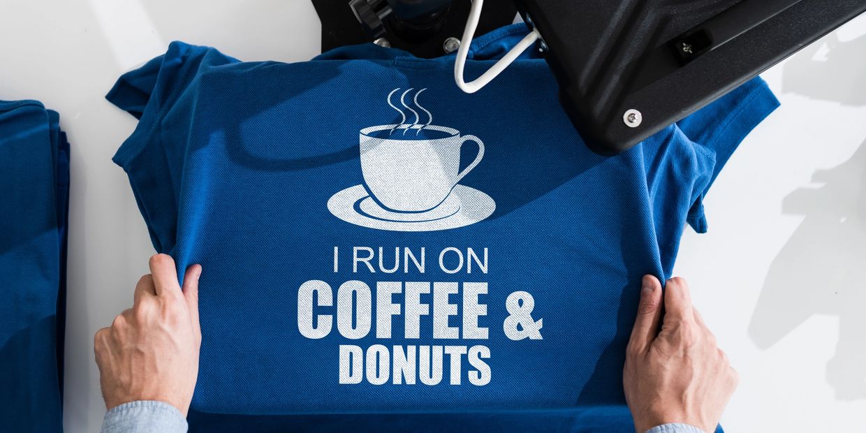Blue t-shirt with “I Run on Coffee & Donuts” design and coffee cup graphic being heat pressed.