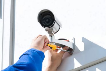 Technician installing a security camera on a building exterior.