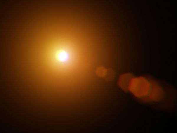 Bright orange light source with lens flare against a dark background.