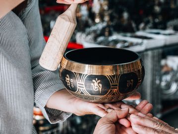 Person playing a traditional Tibetan singing bowl with a wooden mallet.