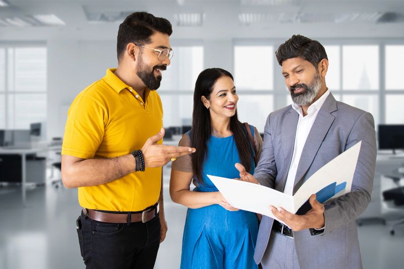 Real estate agent holding file meeting and discussing plan with gus client at his office. Happy young couple interested to buy house or interested in investing in a property
