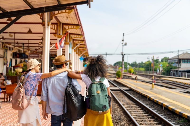 Group of Diversity people tourist travel in Thailand on local train. Man and woman friends traveler waiting for the train during travel on railroad transportation on summer holiday vacations.