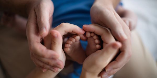 Adult and child hands forming a heart around baby feet.