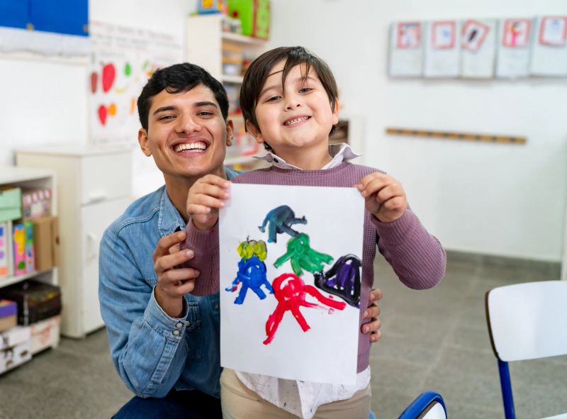 Proud male art teacher and cute student holding his painting showing it while facing the camera smiling very cheerfully - Education concepts