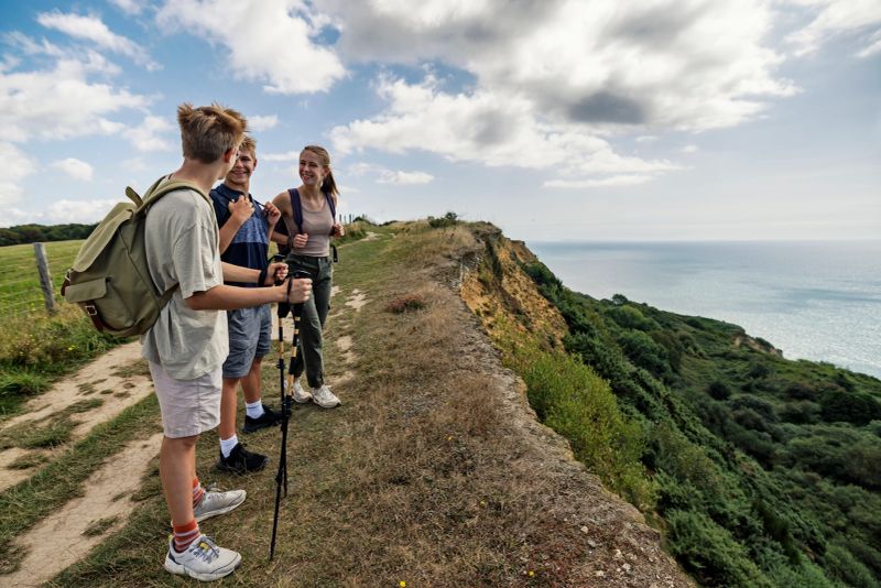 Three teenage kids are hiking in Dorset, United Kingdom. They are standing on cliff by the sea. Kids are looking at the views, talking and laughing.Shot with Canon R5