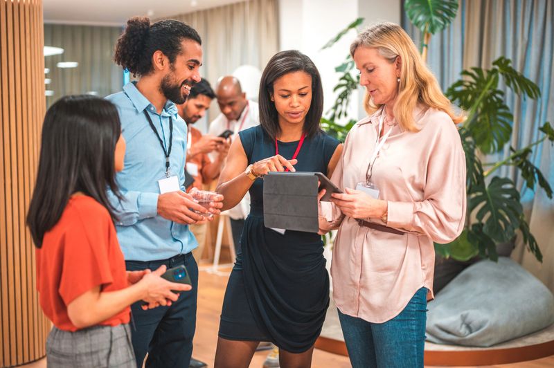 A mix of elegant, multiethnic colleagues converse in a sophisticated corporate environment, employing wireless tools for collaboration.