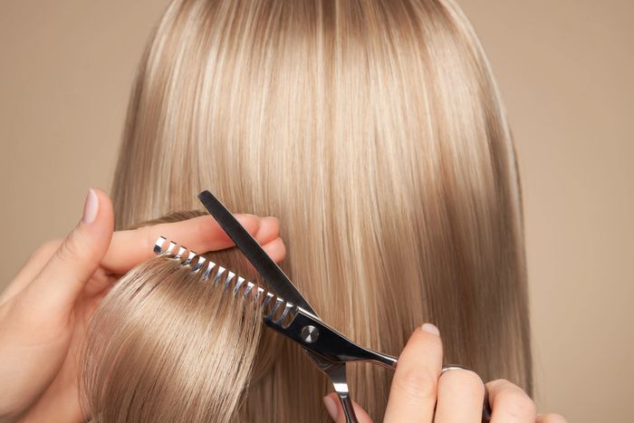 A person trimming blonde hair with thinning scissors for a layered look.
